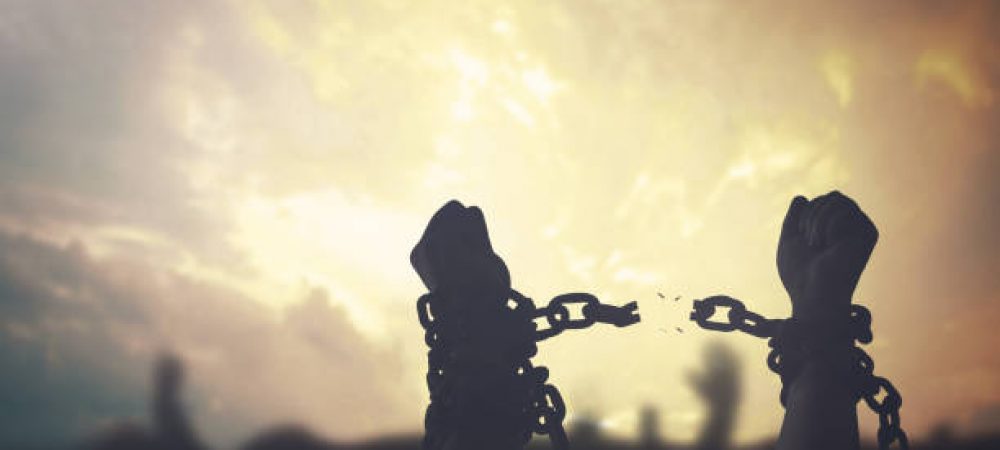 Silhouette human hands raising and broken chains at sunset background